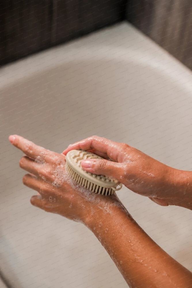 Hands lathering with a round natural rubber body brush over a bath