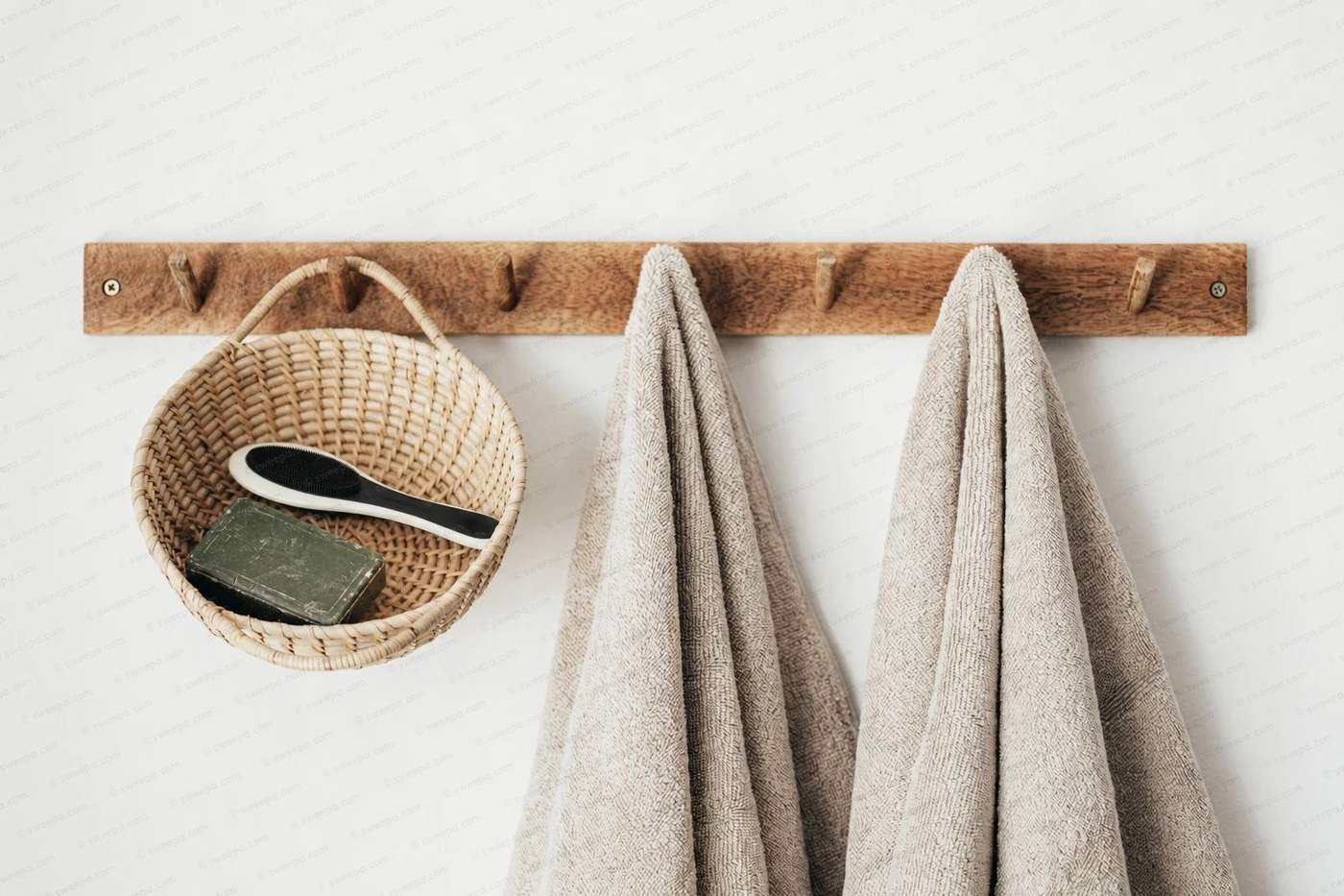 A wooden hook rail with linen towels and a rattan basket holding a natural rubber body brush